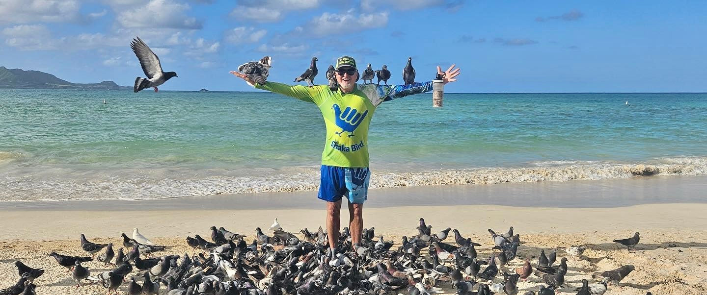 Person standing on a beach with a large group of birds, holding out his arms wide.